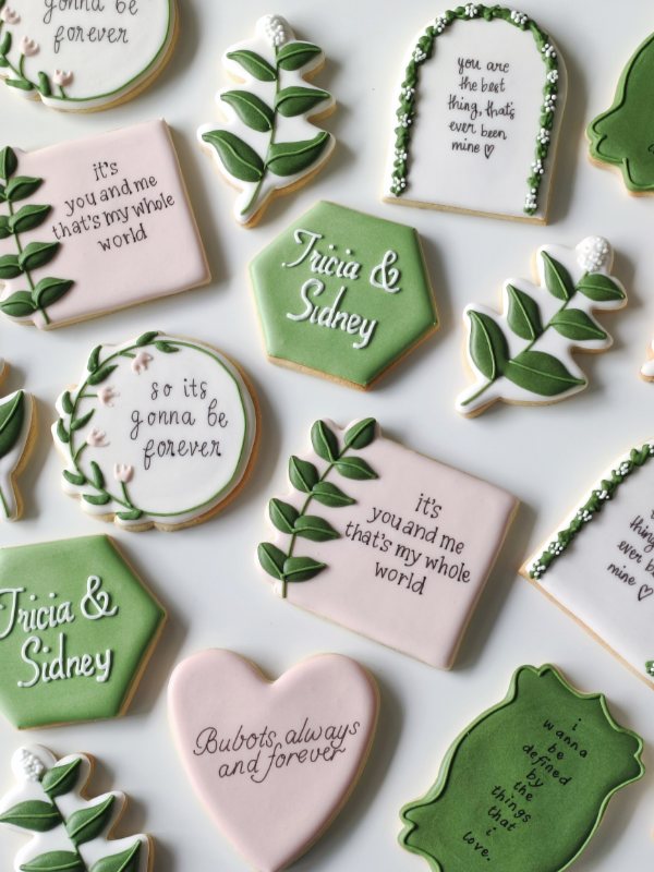 Wedding favour cookies in sage and blush — vine sprigs, lyric plaques and a floral arch
