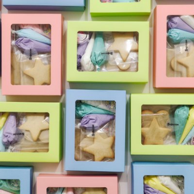 Pastel DIY Cookie Kit boxes in pink, green and blue — star cookies and icing bags peeking through the window lids
