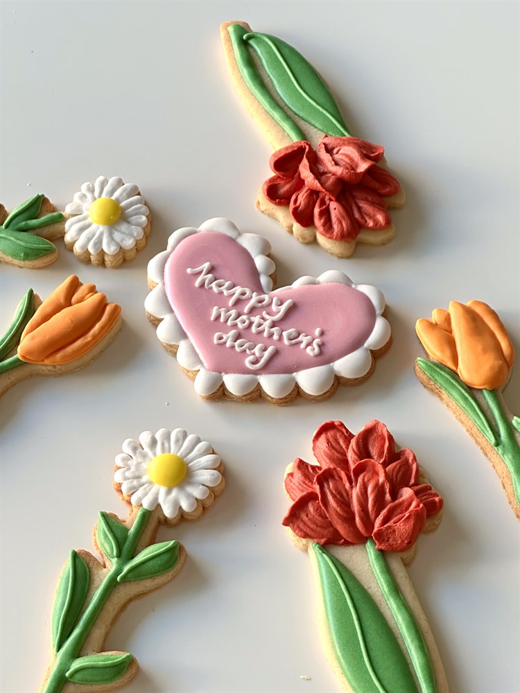 Heart-shaped sugar cookie with hand-piped tulip and daisy bouquet