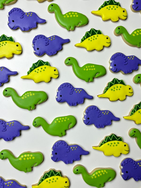 A parade of dinosaur cookies in green, purple and yellow