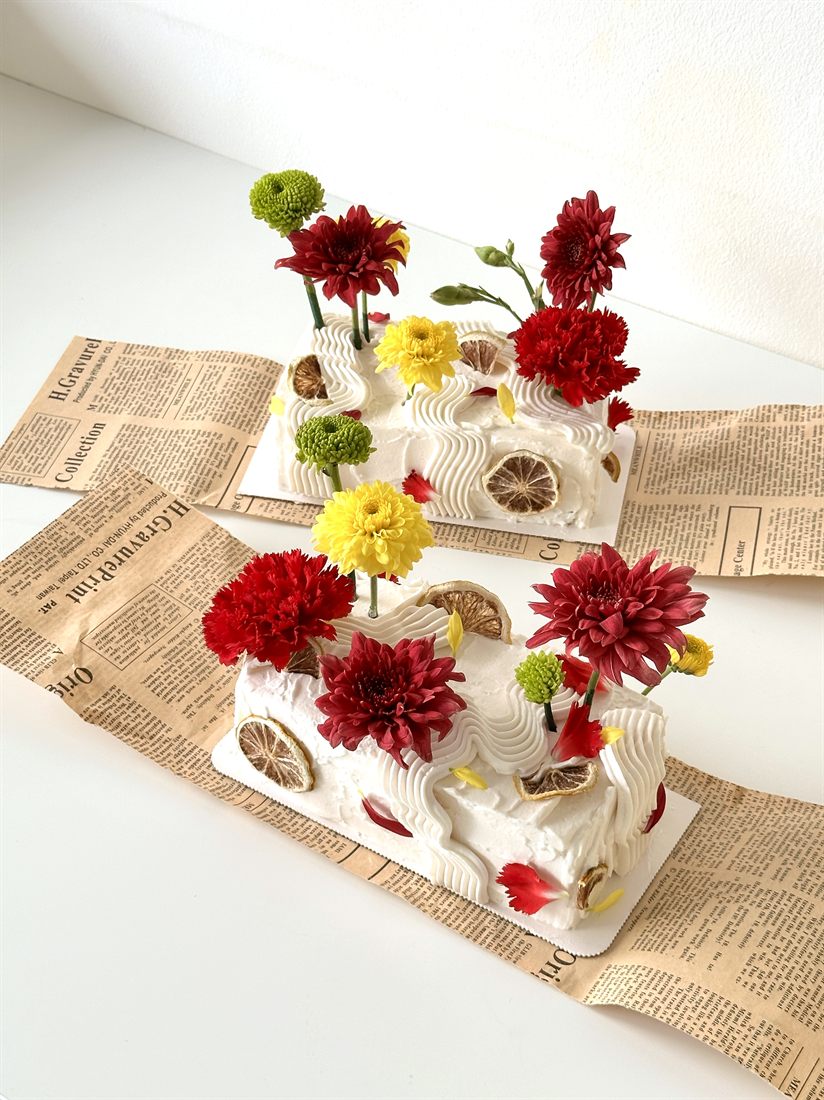 Two Sugarcoat mini slab cakes with piped buttercream waves, real blooms and dried citrus, styled on vintage newspaper