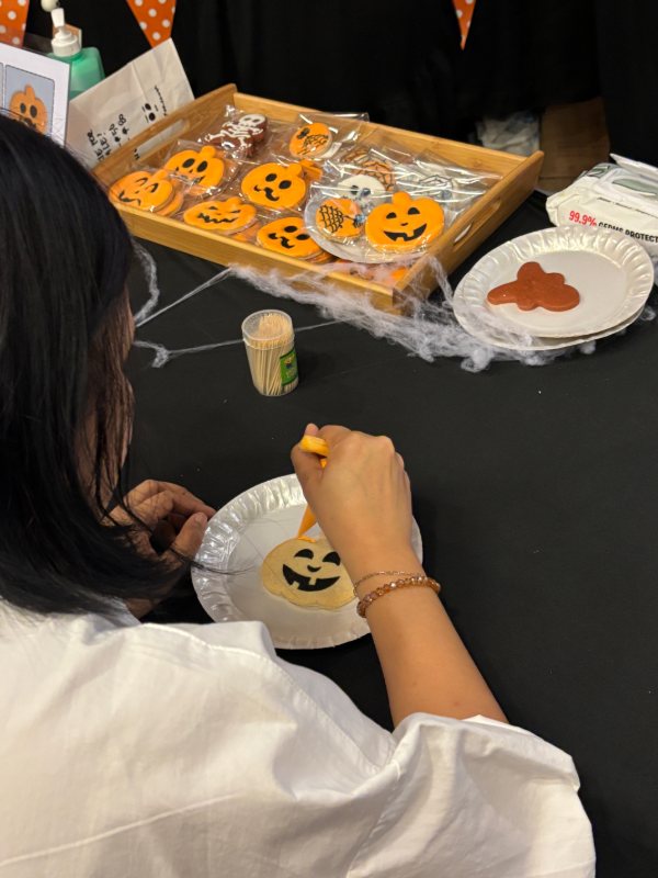 A guest piping a jack-o'-lantern cookie beside the kit tray — icing bags, toothpicks and finished designs